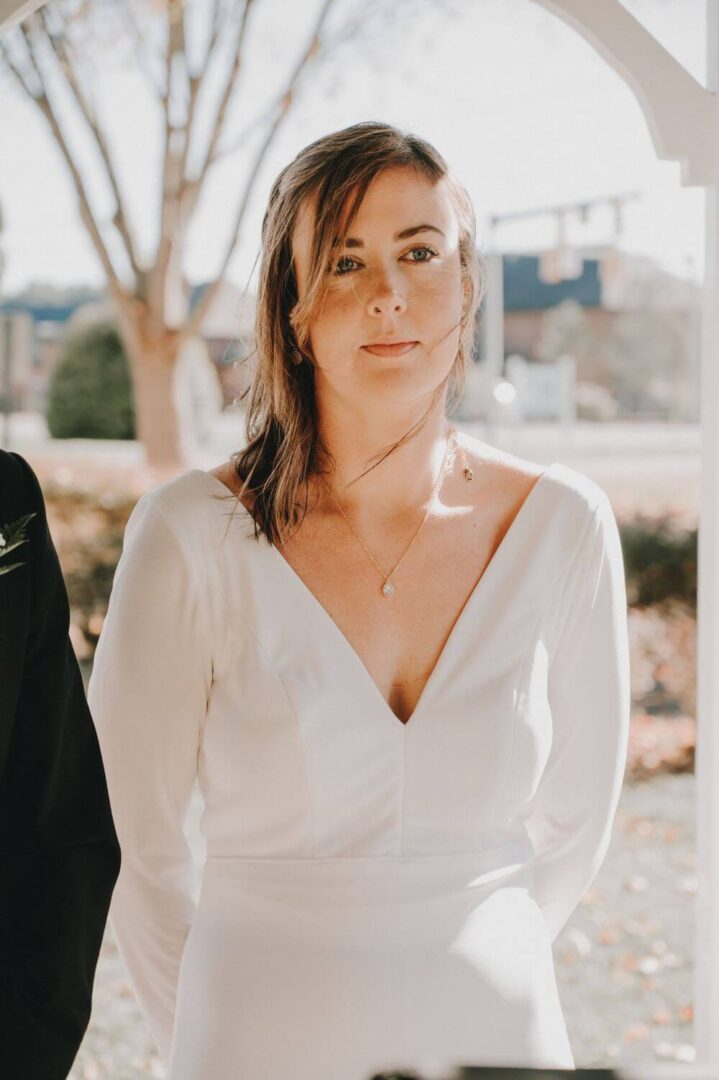 A woman in white dress standing next to a tree.