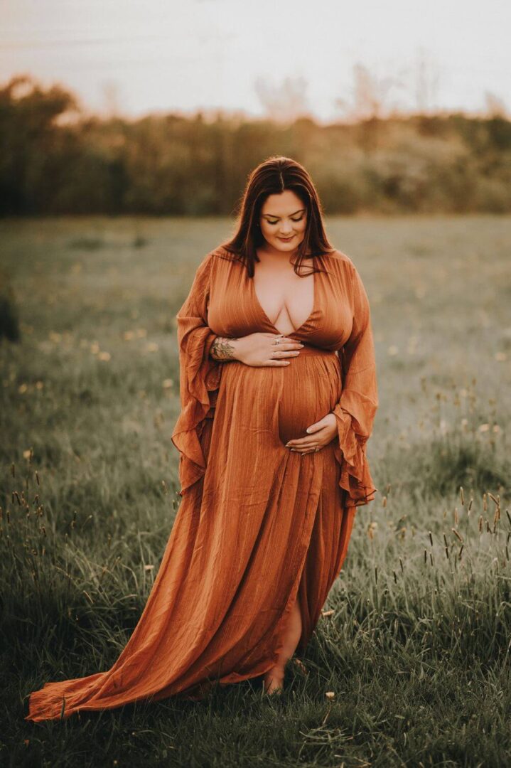 A pregnant woman in an orange dress standing in the grass.