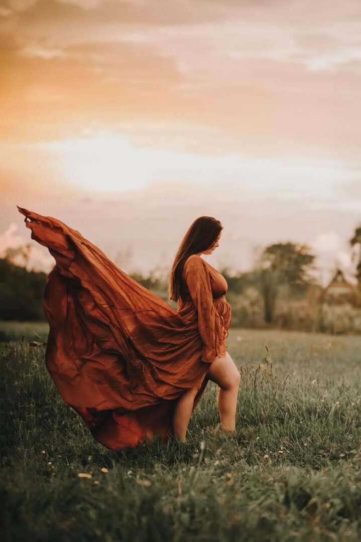 A woman in a red dress is walking through the grass.