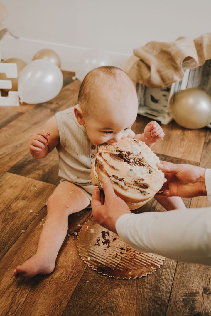 A baby is eating cake while sitting on the floor.