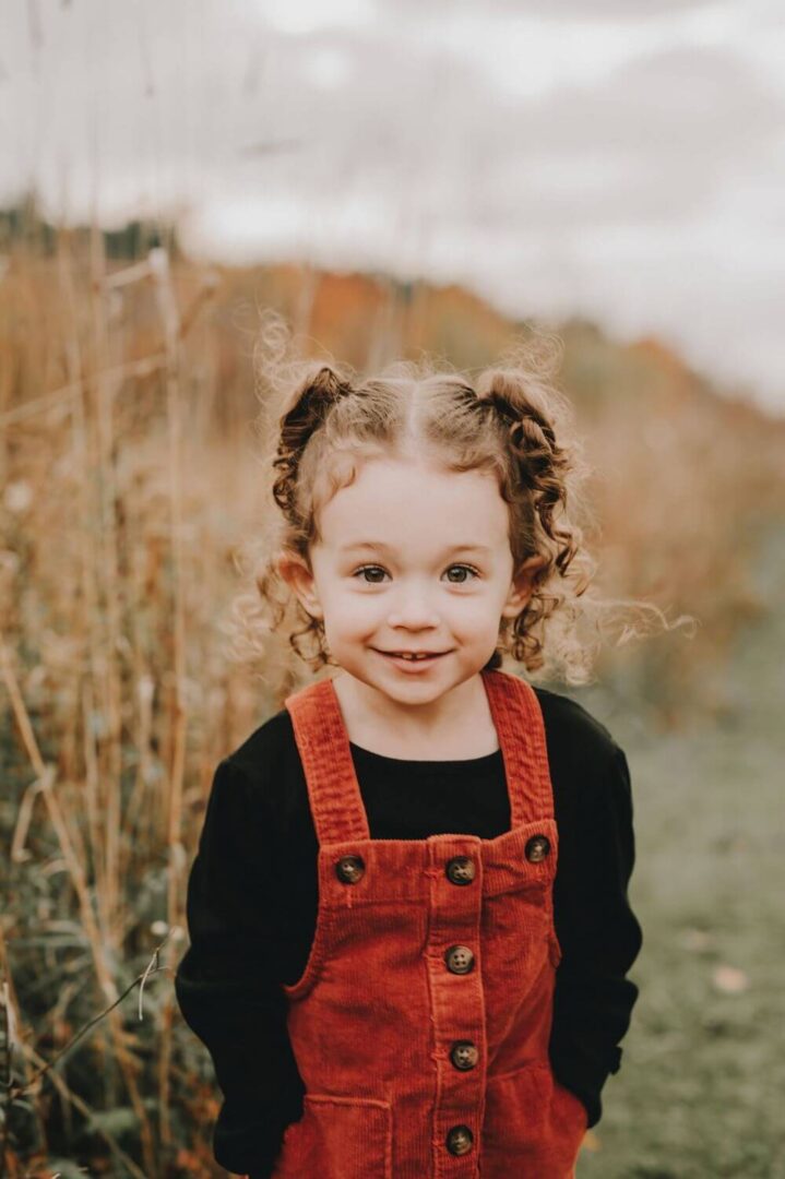 A little girl with pigtails standing in front of some tall grass.