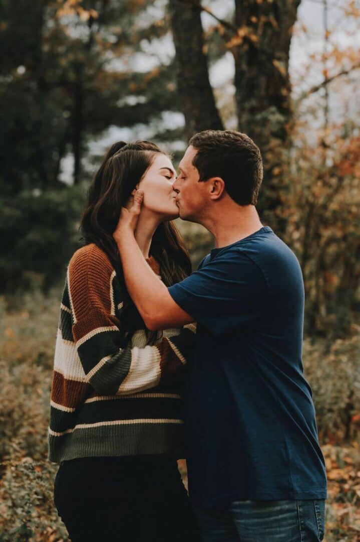 A man and woman kissing in the woods.