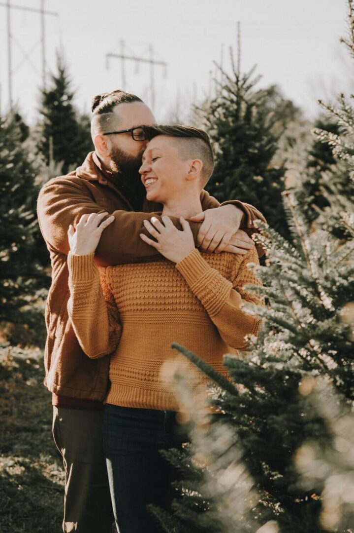 A man and woman hugging in front of trees.