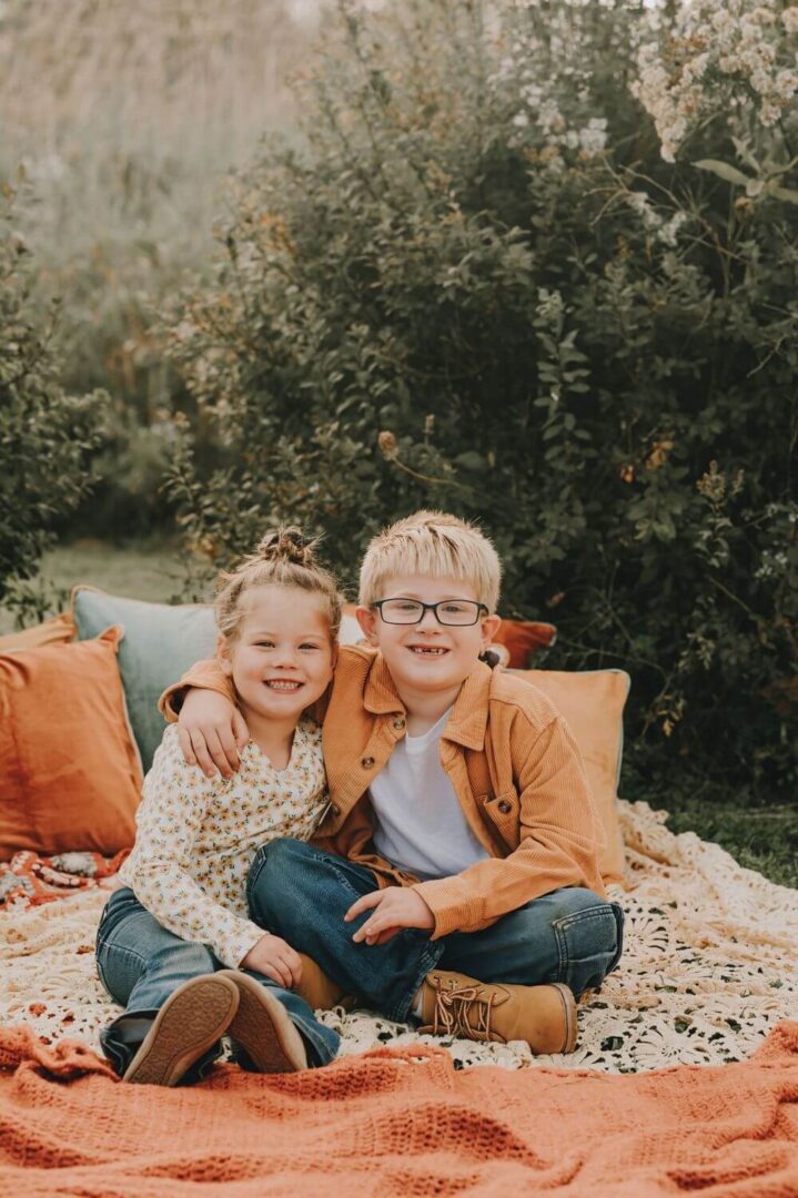 Two children sitting on a blanket in the grass.