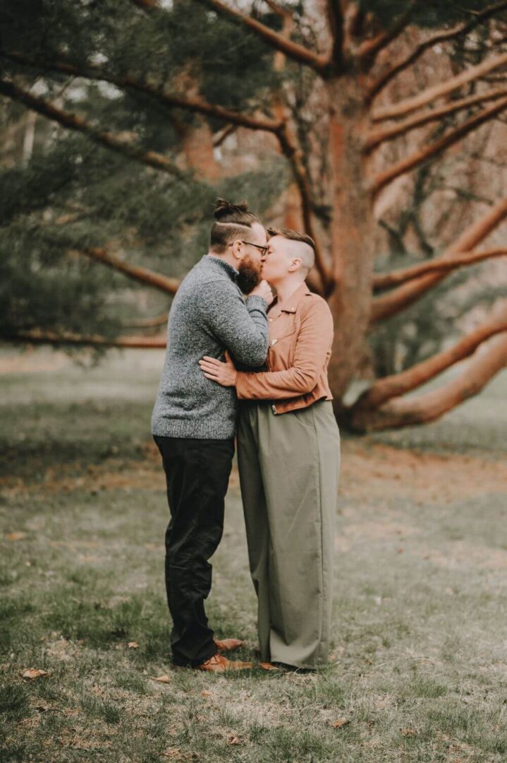 A man and woman kissing in front of a tree.