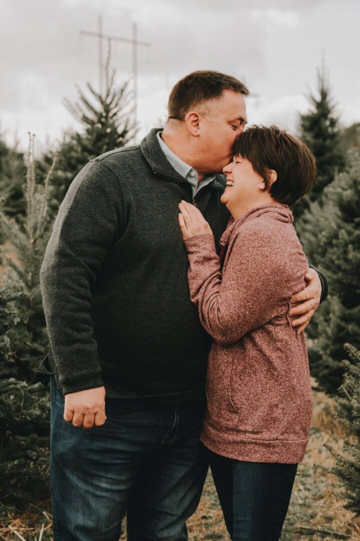 A man and woman kissing in front of trees.