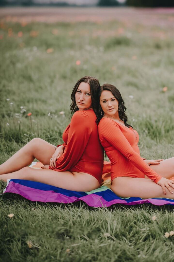 Two women sitting on a blanket in the grass.